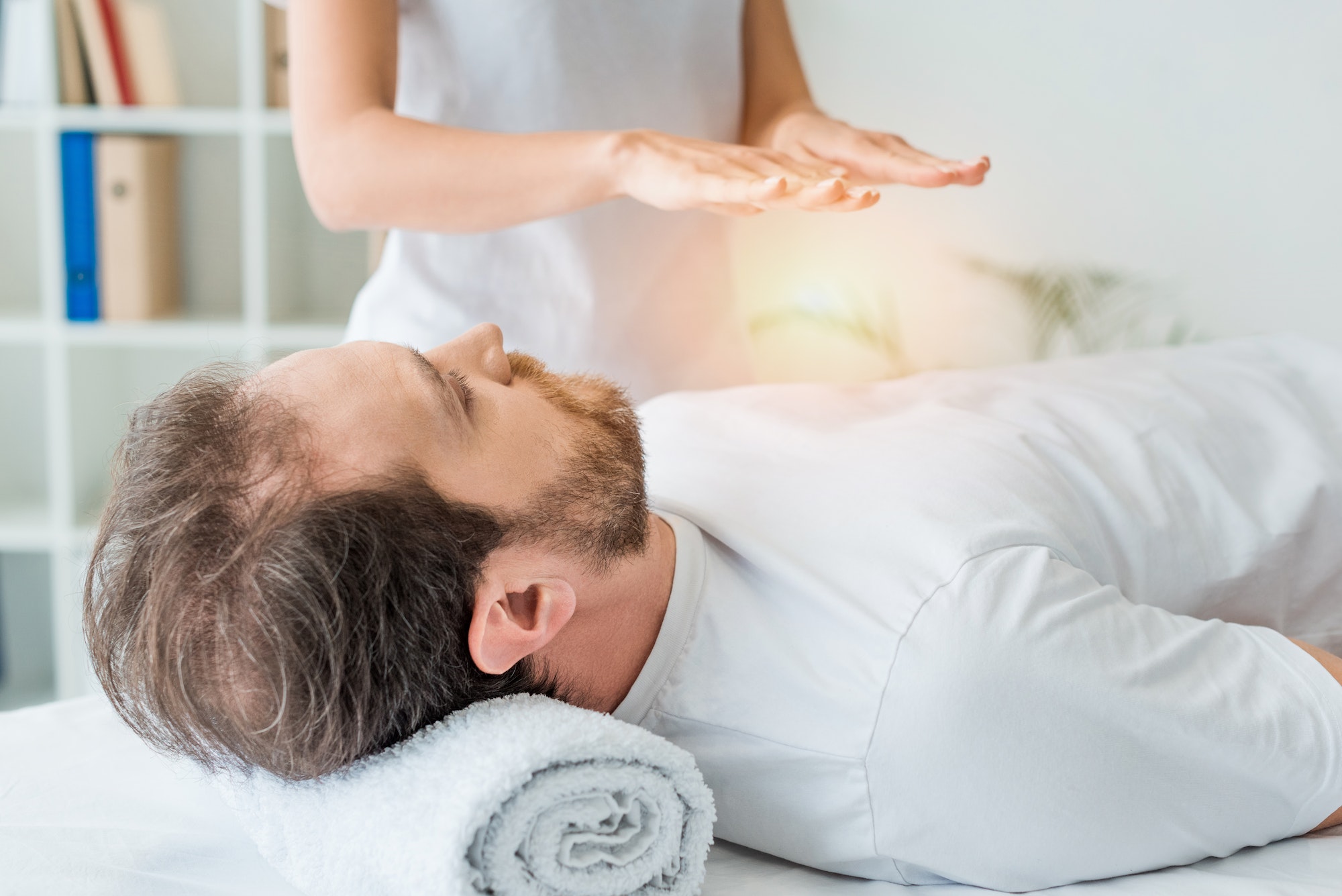 bearded man lying on massage table and receiving reiki treatment